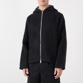 Model wearing Our Legacy Black Zip Through hoodie in textured wool-blend, styled with black trousers, silver zip detail visible.