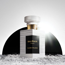 Balmain Blanc Galaxie Eau de Parfum in white ribbed bottle with black label and gold cap, styled on a lunar-inspired surface.