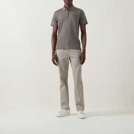Model wearing Calvin Klein Stretch Slim-Leg Chinos in Vintage Khaki, slim-fit with clean hems, styled with a grey polo and white trainers.