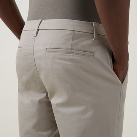 Model wearing Calvin Klein Stretch Slim-Leg Chinos in Vintage Khaki, showing rear jetted pocket and slim-leg fit detail.