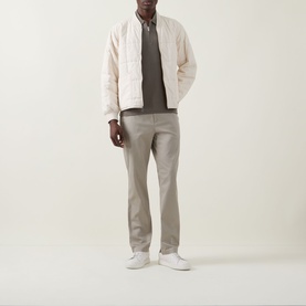 Model wearing Calvin Klein Stretch Slim-Leg Chinos in Vintage Khaki, styled with a cream quilted jacket, grey top, and white trainers.