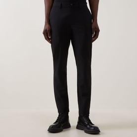Model wearing Calvin Klein Tech Stretch Slim-Leg Trousers in black, slim-leg fit with clean hems, styled with black leather shoes.
