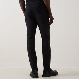 Model wearing Calvin Klein Tech Stretch Slim-Leg Trousers in black, slim-leg fit, shown from rear with black leather shoes.
