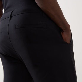 Model wearing Calvin Klein Tech Stretch Slim-Leg Trousers in black, close-up of rear welt pocket and side entry pocket detail.