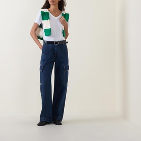 Model wearing Gant Shield Logo T-shirt in white with V-neckline, styled with green striped vest, dark blue wide-leg cargo jeans and black shoes