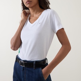 Model wearing Gant Shield Logo T-shirt in white with V-neckline and short sleeves, styled with dark denim jeans and black belt