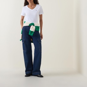 Model wearing Gant Shield Logo T-shirt in white with V-neckline, styled with dark navy wide-leg cargo jeans and a green knitwear waist tie