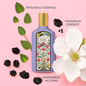 Gucci Flora Gorgeous Magnolia EDP in lilac bottle with gold cap, surrounded by magnolia flower, blackberries, and patchouli leaves on pink background