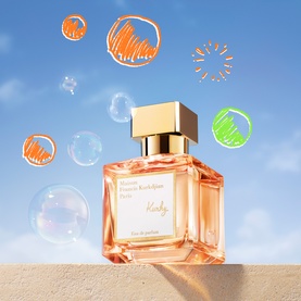 Maison Francis Kurkdjian Kurky Eau de Parfum in a peach glass bottle with gold cap, surrounded by soap bubbles against a blue sky.
