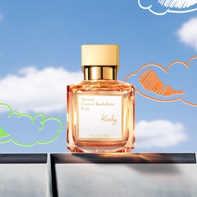 Maison Francis Kurkdjian Kurky Eau de Parfum in amber-tinted bottle with gold cap, set against a sky backdrop with illustrated clouds.
