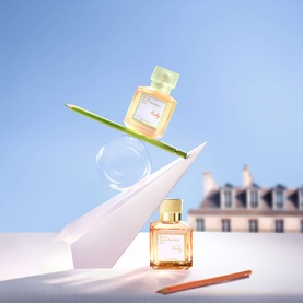 Maison Francis Kurkdjian Kurky Eau de Parfum, two bottles in amber glass with green and gold caps, styled with paper crane and foliage
