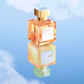 Maison Francis Kurkdjian Kurky Eau de Parfum in amber glass bottle with gold cap, reflected on pastel surface against sky background