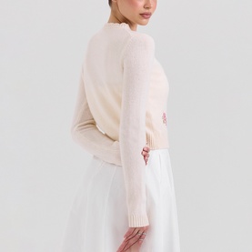 Model wearing House of CB Anjou Knitted Cardigan in Cream Floral with floral embroidery and scallop edges, styled with a white skirt.