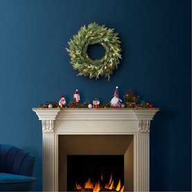 Puleo Arcadia Pre-lit LED Christmas Wreath with warm white lights displayed above a white fireplace mantel decorated with festive figurines