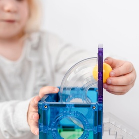 Child placing a yellow ball into Connetix Rainbow Replacement Balls Pack, shown with a blue magnetic tile construction set