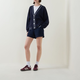 Model wearing Varley navy shorts styled with a matching navy cardigan, white tee, white socks and burgundy trainers.