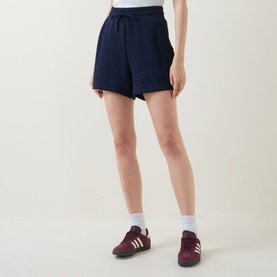Model wearing Varley navy shorts with drawstring waist, styled with burgundy Adidas Gazelle trainers and white socks