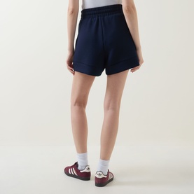 Model wearing Varley navy shorts, rear view, styled with white socks and burgundy Adidas trainers