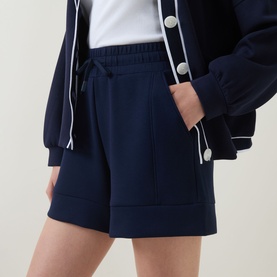 Model wearing Varley navy shorts with elasticated drawstring waist, styled with a matching navy zip-up jacket with white trim detail.