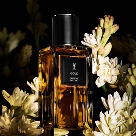 YSL Le Vestiaire des Parfums Gold Eau de Parfum, amber glass bottle with black cap, surrounded by white florals on dark background