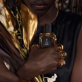 Model with YSL Le Vestiaire des Parfums Gold EDP, holding black and gold bottle, styled with gold rings and necklace