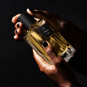 YSL Le Vestiaire des Parfums Trench Eau de Parfum held in two hands, amber liquid in a rectangular black-capped glass bottle
