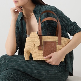 Model carrying Loewe Elephant Raffia Basket Bag in natural/tan, woven raffia with tan leather elephant detail and short top handles