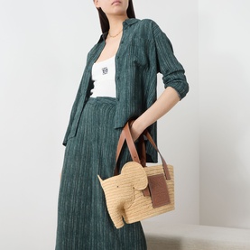 Model carrying Loewe Elephant Raffia Basket Bag in natural/tan with brown leather handles and trims, styled with green co-ord set