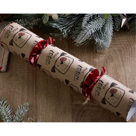 Robin Reed Dog Singular Christmas Cracker in kraft paper with dog motif print, red satin ribbons, styled with festive pine branches on wooden surface