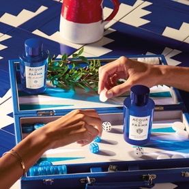 Acqua di Parma Mirto di Panarea La Riserva EDP 50ml in blue bottles styled on a blue backgammon board with botanicals and red jug