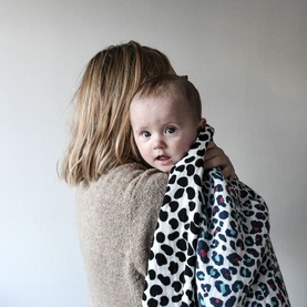 Baby held over shoulder wrapped in Etta Loves Animal Print Reversible Muslin Blanket, showing Dalmatian print side in black and white multi colourway