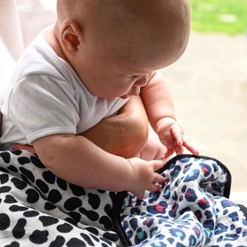 Baby wrapped in Etta Loves Animal Print Reversible Muslin Blanket, showing Dalmatian and Blue Leopard print sides in multi colourway