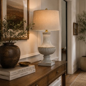 Mindy Browne Sariq Ceramic Table Lamp in cream beige with ribbed urn base and linen drum shade, styled on wooden sideboard with vase and artwork.