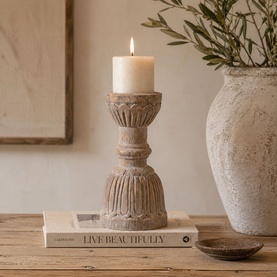 Mindy Browne Fera Candle Holder in beige ceramic with carved column detailing, styled with a lit pillar candle on a wooden surface.
