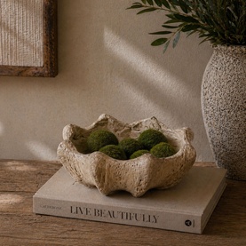 Textured stone-effect decorative bowl in cream, filled with moss balls, styled on a coffee table book in a warm neutral setting