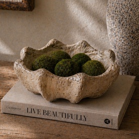 Mindy Browne Lakota Shell Small Bowl in cream sand ceramic, filled with decorative moss balls, styled on a coffee table book.