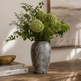 Mindy Browne Helton Large Vase in brown-grey textured ceramic, styled with green hydrangeas on a wooden surface beside stacked books.