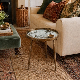 Mindy Browne Japanese Garden Round Side Table in gold with marble-effect glass top on slim legs, styled in a cosy living room setting.