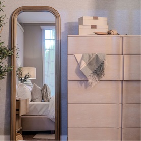 Mindy Browne Louis Large Mirror in gold arched frame, styled in a bedroom setting beside a white textured chest of drawers