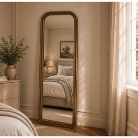 Mindy Browne Louis Large Mirror in gold, arched full-length frame leaning against wall in styled bedroom setting