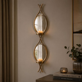 Mindy Browne Claude Mirror Double Wall Sconce in gold, two oval mirrored panels with fish-tail iron frame, wall-mounted with lit candles