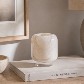 Small cream marbled glass vase with clear base, styled on a book beside a bowl and framed artwork in a natural home setting.