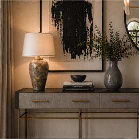 Mindy Browne Ashford Large Bird Table Lamp in grey gold ceramic, styled on a dark console table with books, bowl, and foliage vase.