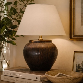 Mindy Browne Orna Table Lamp in brown ceramic with white empire shade and gold detail, styled on books beside framed art and greenery.