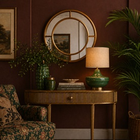 Mindy Browne Adele Round Mirror in gold, styled above a ribbed console table with green ceramic lamp and decorative vases in a warm-toned room