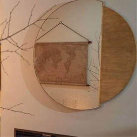 Large round wall mirror with gold-toned wooden panel backing, styled with a vintage world map hanging scroll and decorative branches