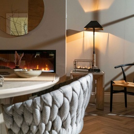 Chunky knit grey curved sofa in styled living space with lit fireplace, table lamp, and wooden flooring