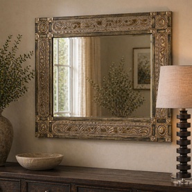 Mindy Browne Christoph Rectangular Mirror in brown gold with ornate carved metal frame, styled on a wooden sideboard with lamp and foliage.