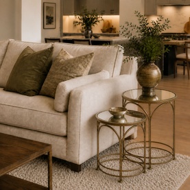 Mindy Browne Ethan Round Nest of Tables Two-Piece Set in gold, iron frames with glass tops, styled beside a cream sofa with green cushions