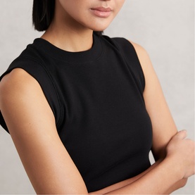 Model wearing Reiss black sleeveless top with structured shoulder detail, arms crossed, neutral background.